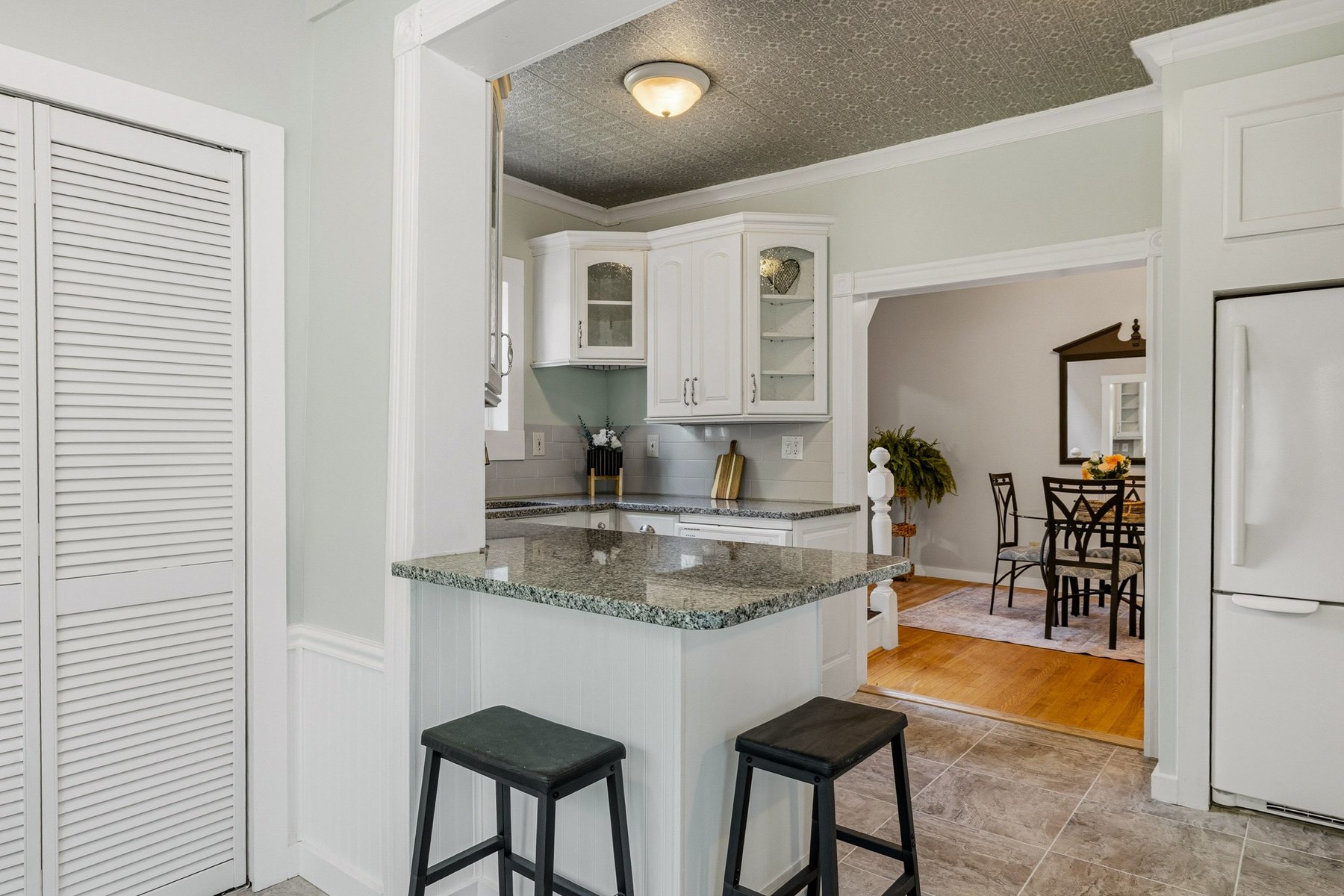 Historic side kitchen with granite breakfast bar, white shaker cabinetry and original pressed-tin ceiling