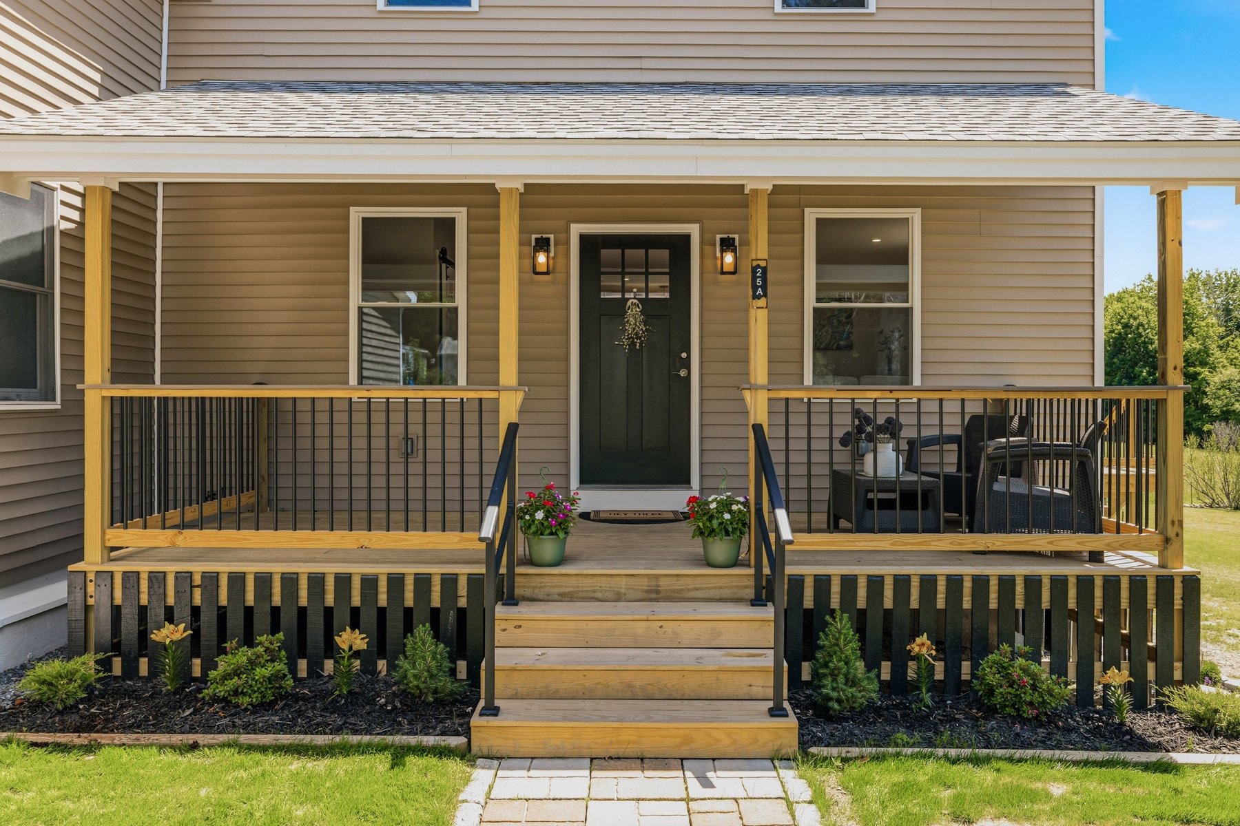 Farmer's porch entry of the new-build Side A with potted flowers, porch seating and a stone walkway